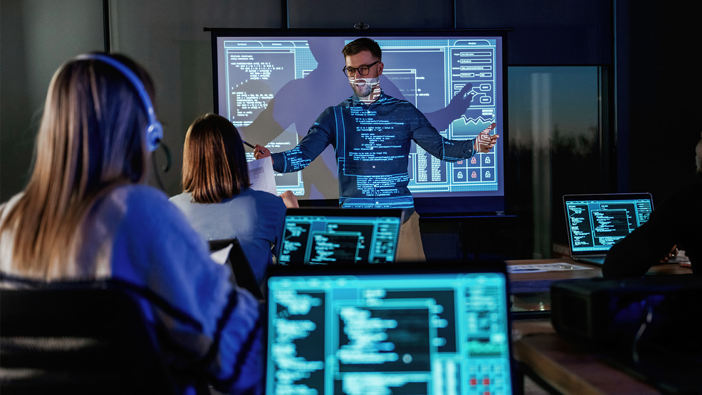 Studerande med bärbara datorer. Lärare framför projektor med data. Undervisning.